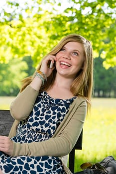Laughing teenage girl talking on the phone sitting in park