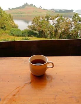 A cup of coffee sitting on a table overlooking a tropical lake view