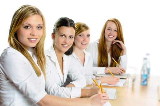 Four young women sitting at a table and hold a pencil in hand, they look happy in the camera, isolated against a white background.