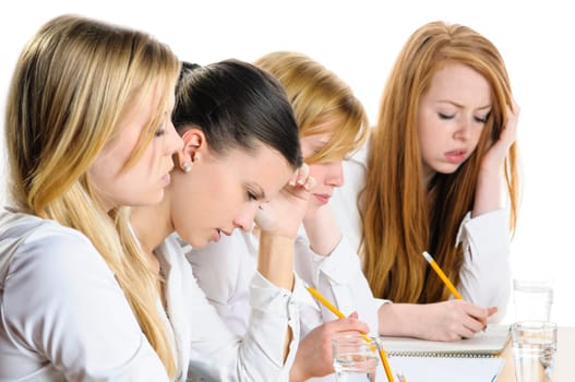 Four young women sitting at a table and write a focused examination, isolated against white background.