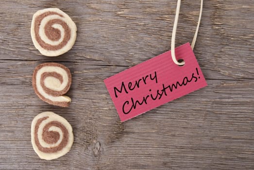 merry christmas written on a red tag with some cookies on a wooden background