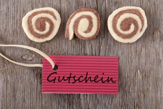 a red label with the german word Gutschein which means voucher on it and some cookies on a wooden background