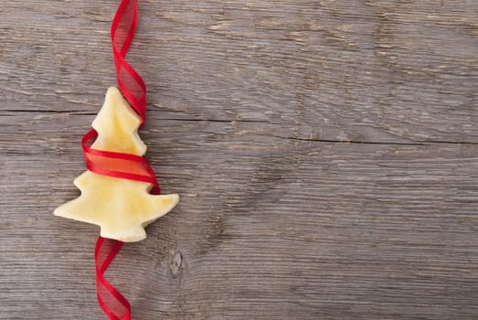 a blank christmas tree cookie wrapped in red ribbon on wood as background with copy space