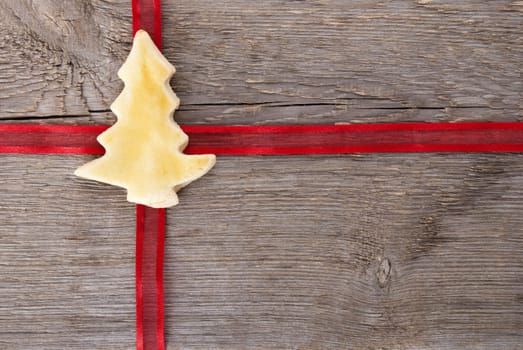 a red ribbon as on a gift with a christmas tree cookie in the middle on wood as background