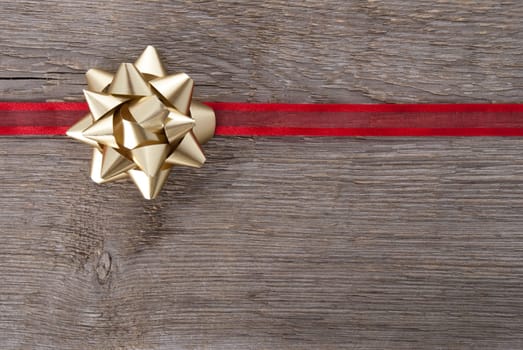 a golden bow on a red ribbon on wood as background with copy space