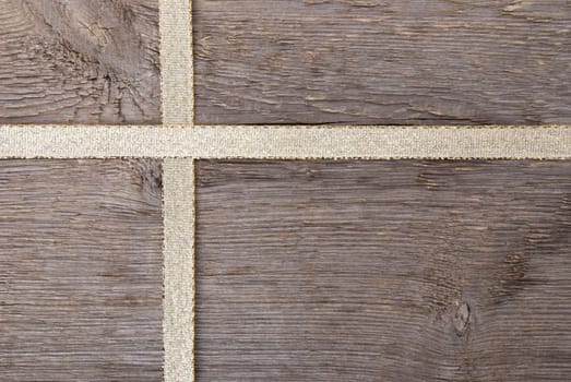 golden ribbon in form of a cross on wood as gift background