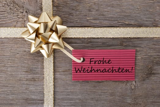 the german words Frohe Weihnachten which means merry christmas on a red label on a golden bow as background