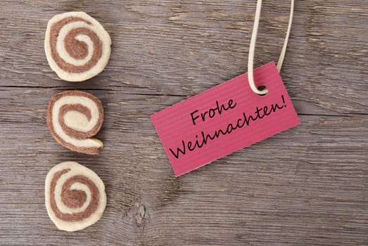 the german words Frohe Weihnachten which means merry christmas on a red label with cookies as background