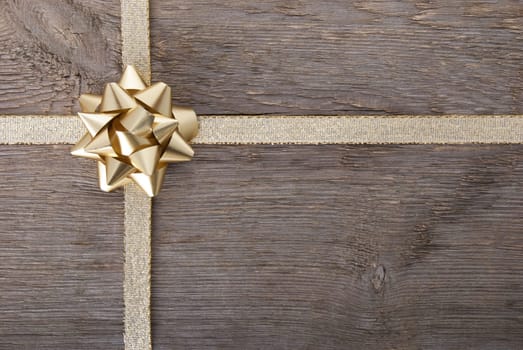 a golden bow on golden ribbon on wood as background with copy space