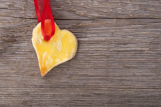 a baked heart with copy space hanging on red ribbon on wooden background