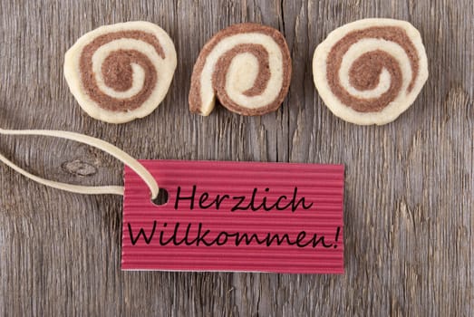 the german words Herzlich Willkommen which means welcome on a red label with cookies on wooden background