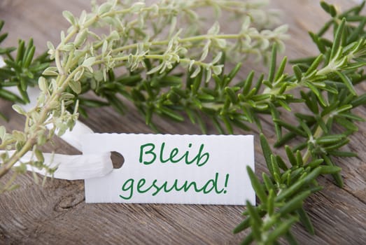 a white label with the german words Bleib gesund which means stay healthy with herbs in the background