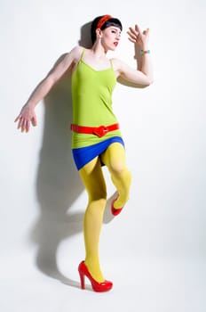 Young woman with black straight hair wears colorful mixed clothes and stands in front of a white background.
