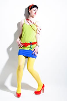 Young woman with black straight hair wears colorful mixed clothes and stands in front of a white background.