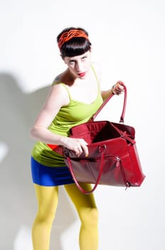 Young woman with black straight hair wears colorful mixed clothes and stands in front of a white background.
