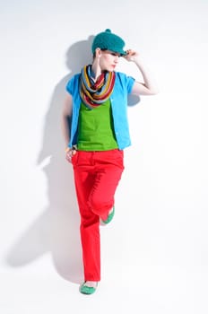 Young woman with black straight hair wears colorful mixed clothes and stands in front of a white background.