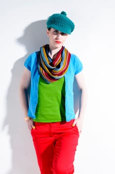 Young woman with black straight hair wears colorful mixed clothes and stands in front of a white background.