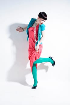 Young woman with black straight hair wears colorful mixed clothes and stands in front of a white background.