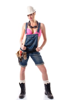 Young attractive woman wears denim dungarees,a tool belt and an orange construction helmet and stands in front of a white background.