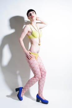 Young woman with black straight hair wears colorful mixed clothes and stands in front of a white background.