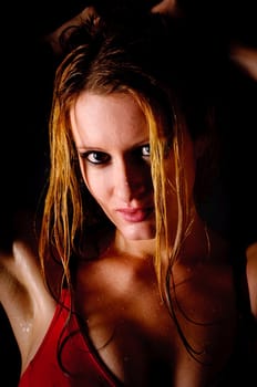 Attractive young woman with long blonde hair in a tight sports dress is still sweaty from sports and stands in front of a black background.