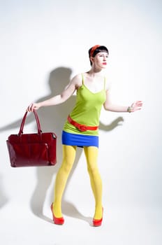 Young woman with black straight hair wears colorful mixed clothes and stands in front of a white background.