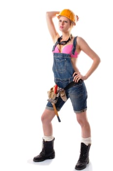 Young attractive woman wears denim dungarees,a tool belt and an orange construction helmet and stands in front of a white background.