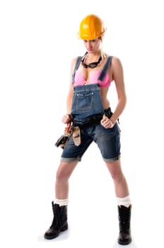 Young attractive woman wears denim dungarees,a tool belt and an orange construction helmet and stands in front of a white background.