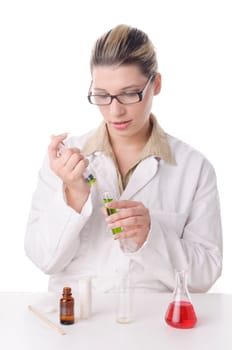 Attractive young chemical laboratory assistant with blond hair and glasses works with various colored liquids in test tubes,exposed against a white background. On the table are various colored chemicals.