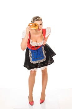 Young attractive woman with blond hair and braids wears a colorful dirdl dress and holds a pretzel in her hand,exposed against a white background.