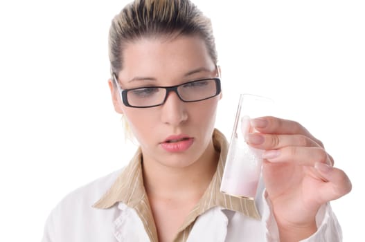 Young pretty woman wears a white coat and glasses. She holds a large test tube with a white liquid in her hand and looks intently,exposed against a white background.