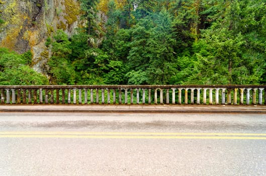 Concrete railing of historic Highway 30 with a beautiful green rainforest passing through the Columbia River Gorge in Oregon.