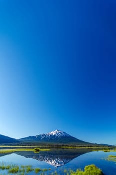 Mount Bachelor being reflected in a lake with most of the image being taken up by beautiful blue sky