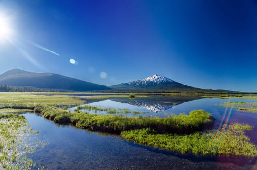 Mount Bachelor being reflected in a lake with a lens flare near Bend, Oregon