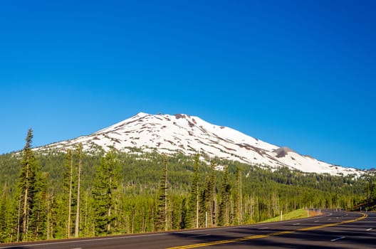 A highway leading through a forest passing next to snowy Mount Bachelor near Bend, Oregon