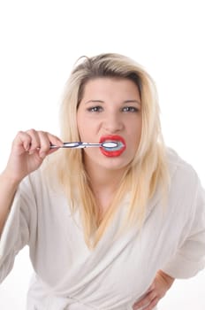 Attractive young woman with long blonde hair wears a white bathrobe and brushes her teeth with a toothbrush,exposed against a white background.