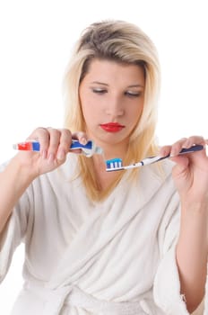 Attractive young woman with long blonde hair wears a white bathrobe and brushes her teeth with a toothbrush,exposed against a white background.