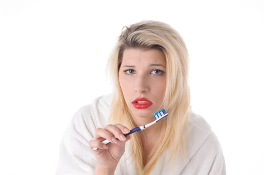 Attractive young woman with long blonde hair wears a white bathrobe and brushes her teeth with a toothbrush,exposed against a white background.