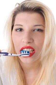 Attractive young woman with long blonde hair wears a white bathrobe and brushes her teeth with a toothbrush,exposed against a white background.