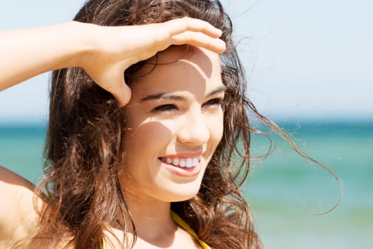 summer woman on the beach looking far away. holding her arm near her eyes.