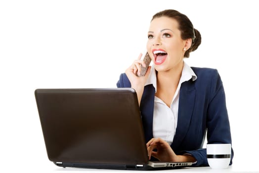 smiling young business woman speaking on phone while using a laptop,isolated on white