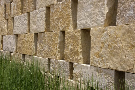 Background of a beige natural stone wall with green grass in front