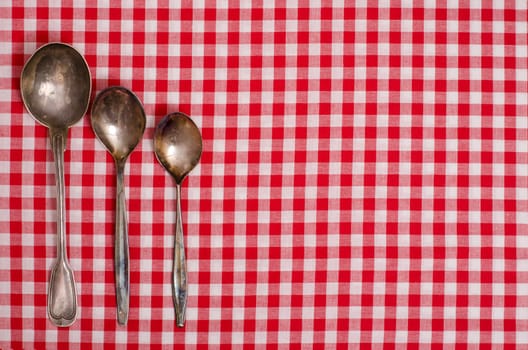 Three silver spoons on a table with red checkered cloth