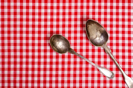Two old silver spoons on a red and white checkered tablecloth