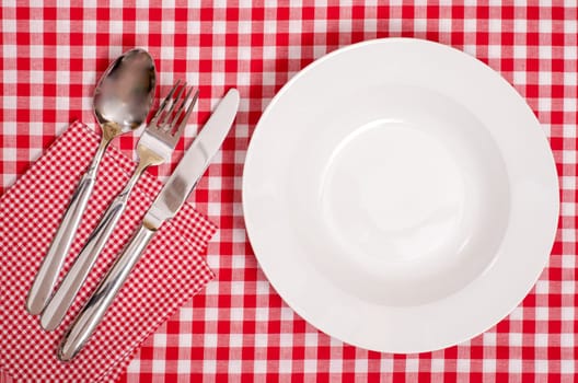 White plate and cutlery made of spoon,knife and fork with checkered napkin