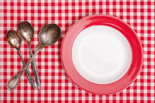 Three spoons made of silver and red plate on checkered cloth