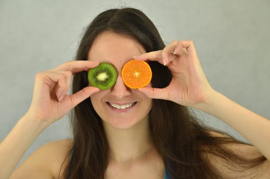 Beautiful young girl is holding tangerine and kiwi