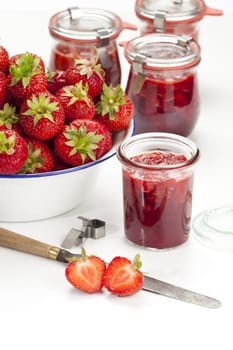 Freshly harvested strawberries in a white enamel bowl and homemade jam in jars against a white background