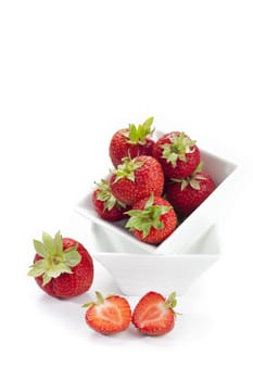 Sugar-sweet strawberries in a white porcelain bowl and two half strawberries in front of it insulated against a white background