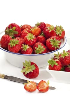 New strawberries in a white porcelain bowl and an enamel bowl with a knife in front of it,insulated against a white background